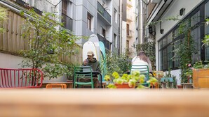 An outdoor seating area with tables and chairs, surrounded by potted plants and a red metal barrier. - Koba Hostel (San Sebastián)