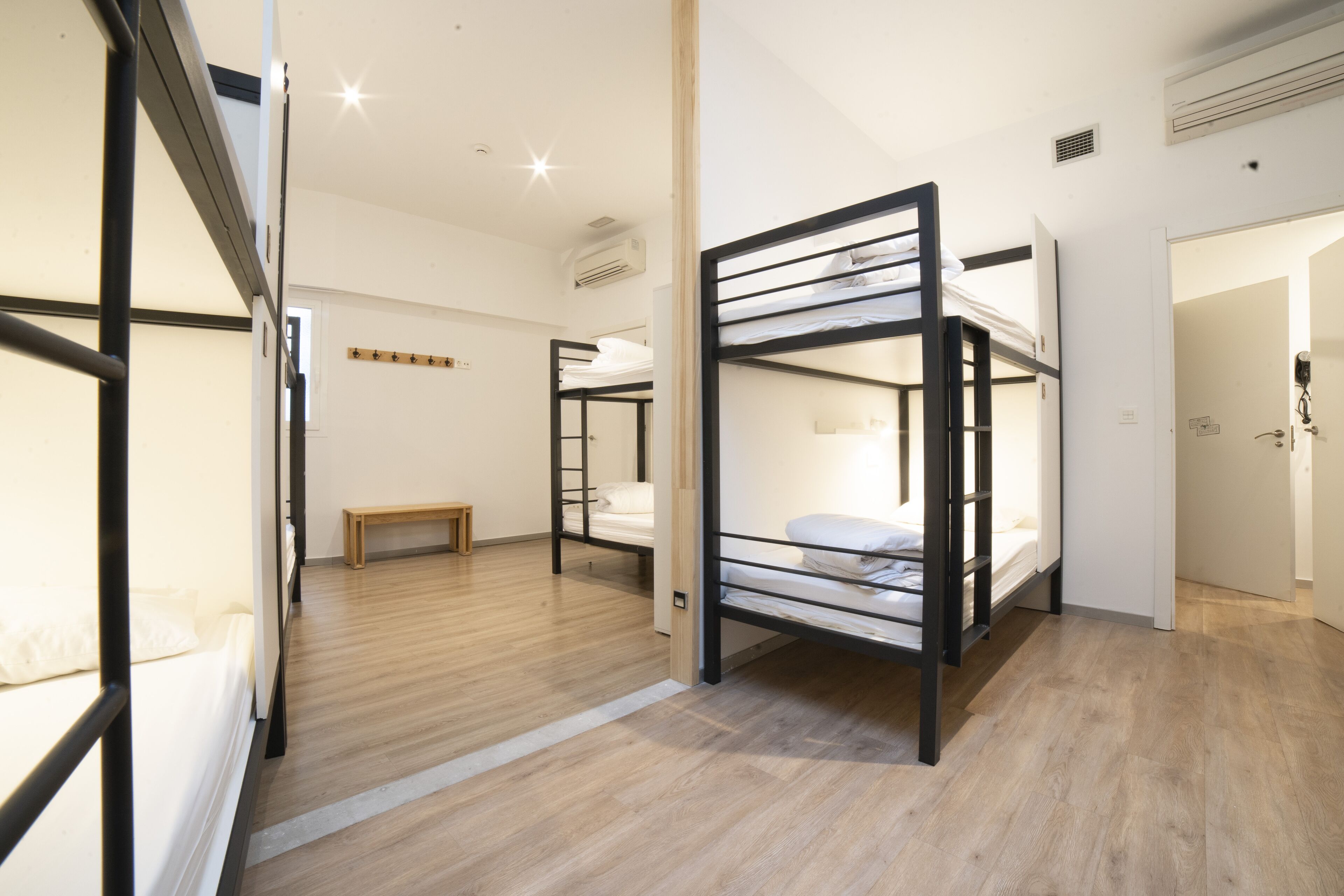 A modern, well-lit room with bunk beds, a wooden floor, and a bench.