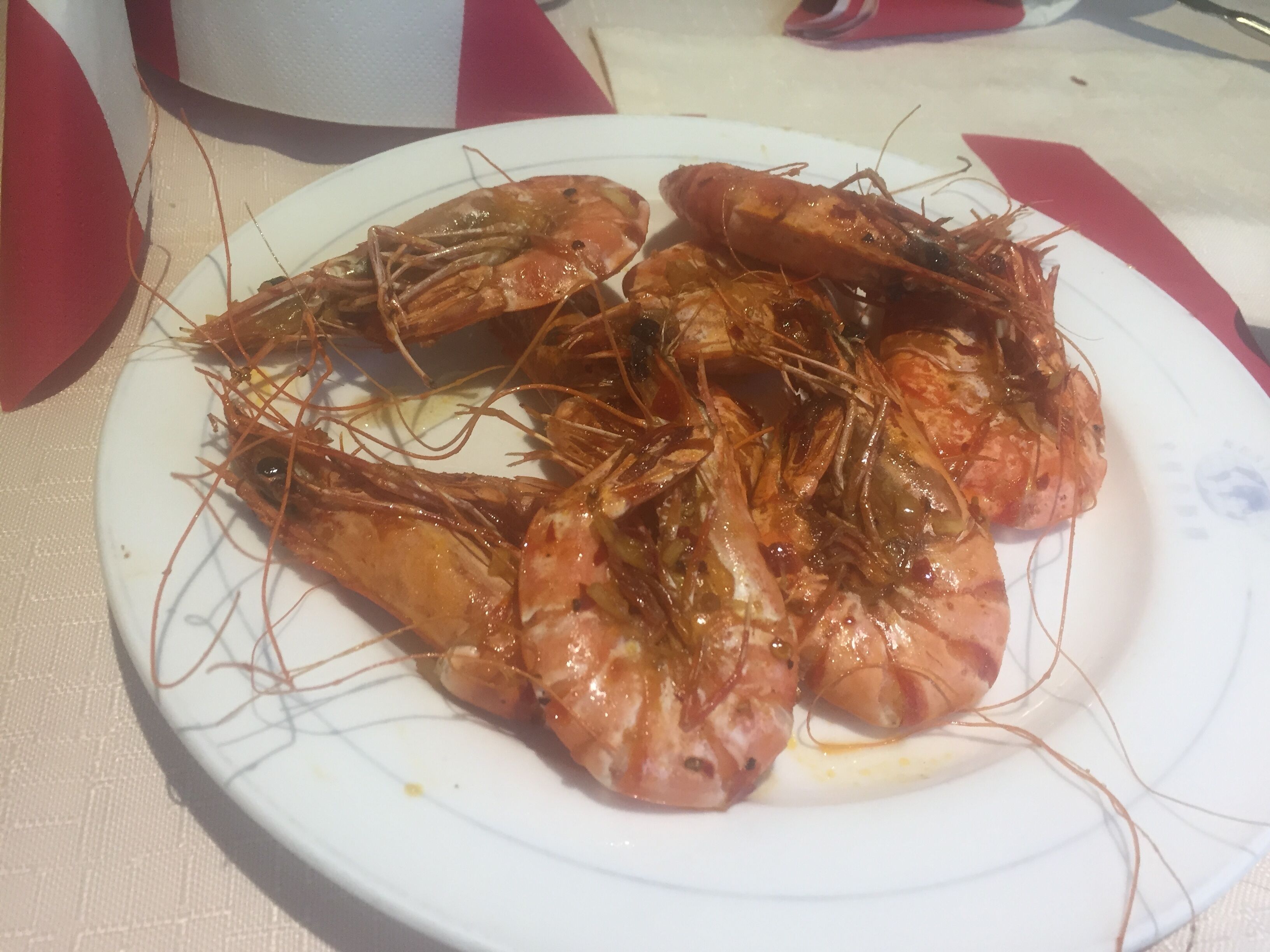 En tallerken med dampende rejer i blank sauce, serveret på en hvid tallerken med rødt mønster.