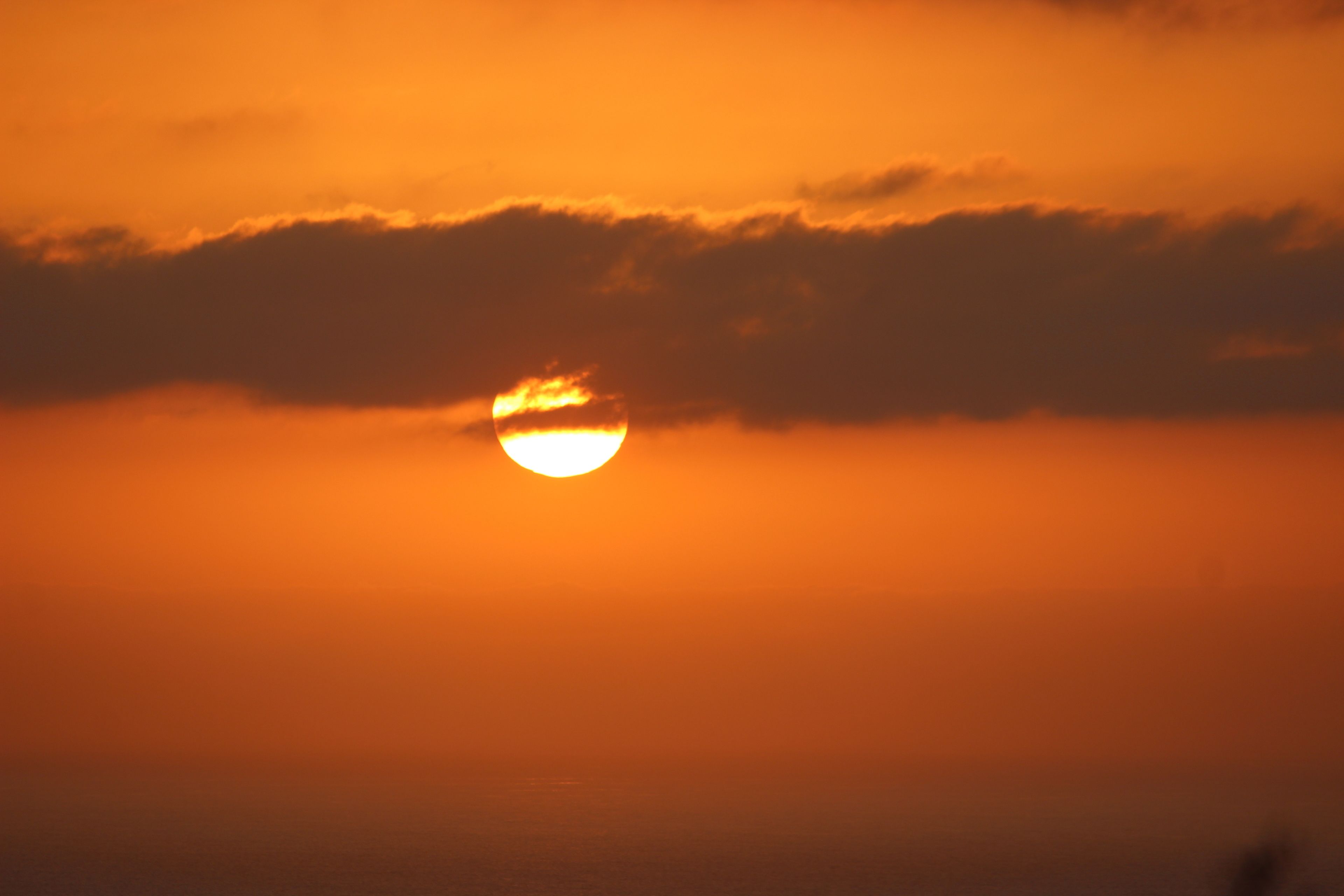 A sunset with the sun partially obscured by clouds.