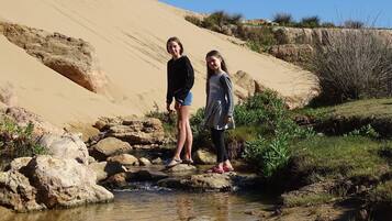 Duas pessoas perto de um riacho em uma paisagem desértica, com dunas de areia ao fundo.
