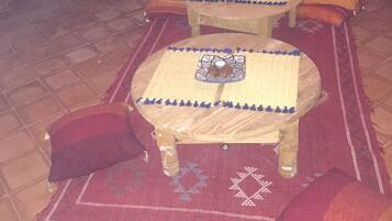 A room with two wooden tables, red and orange cushions, and a patterned rug.
