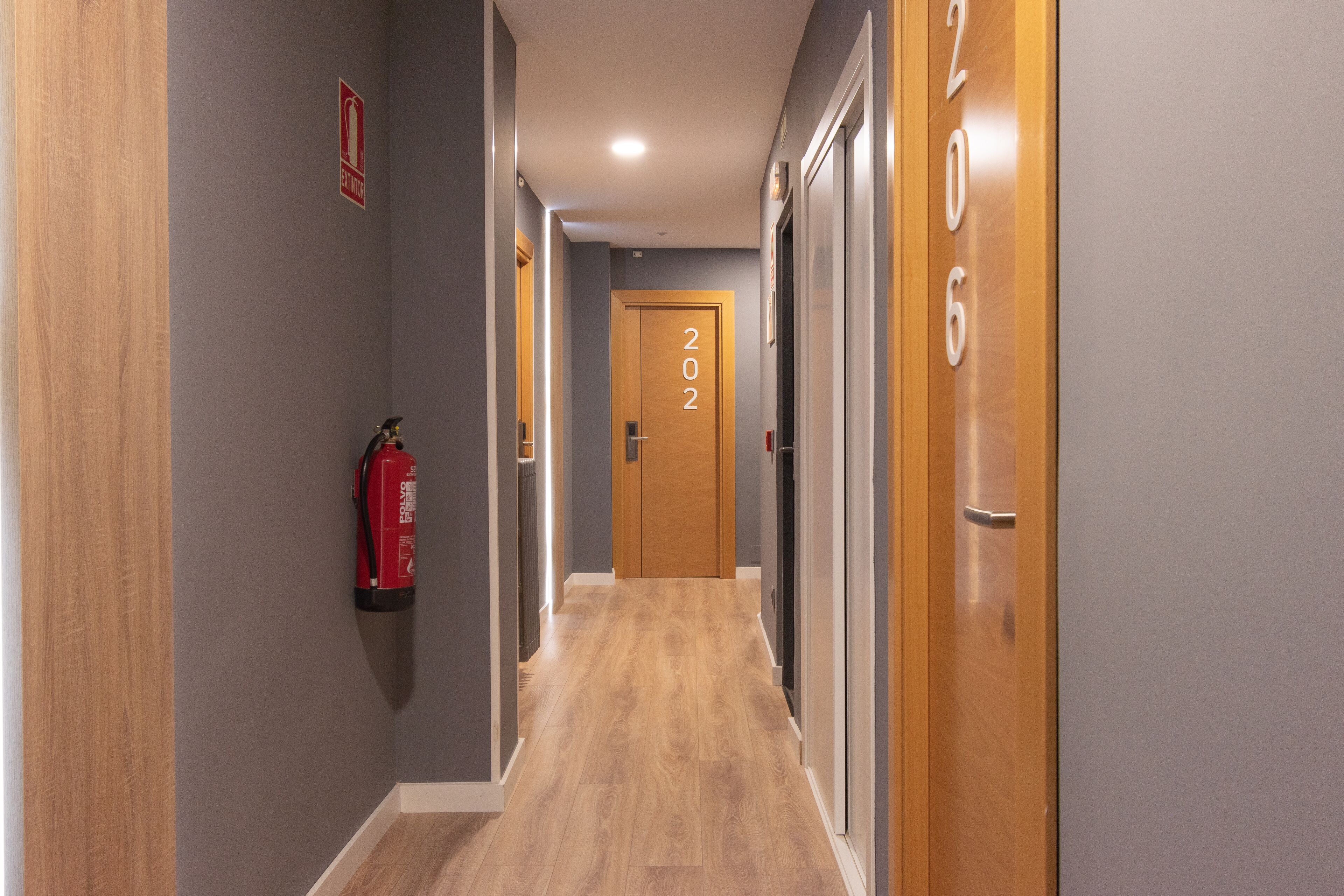 A hallway with wooden flooring, a fire extinguisher on the left, and doors numbered 202 and 206.
