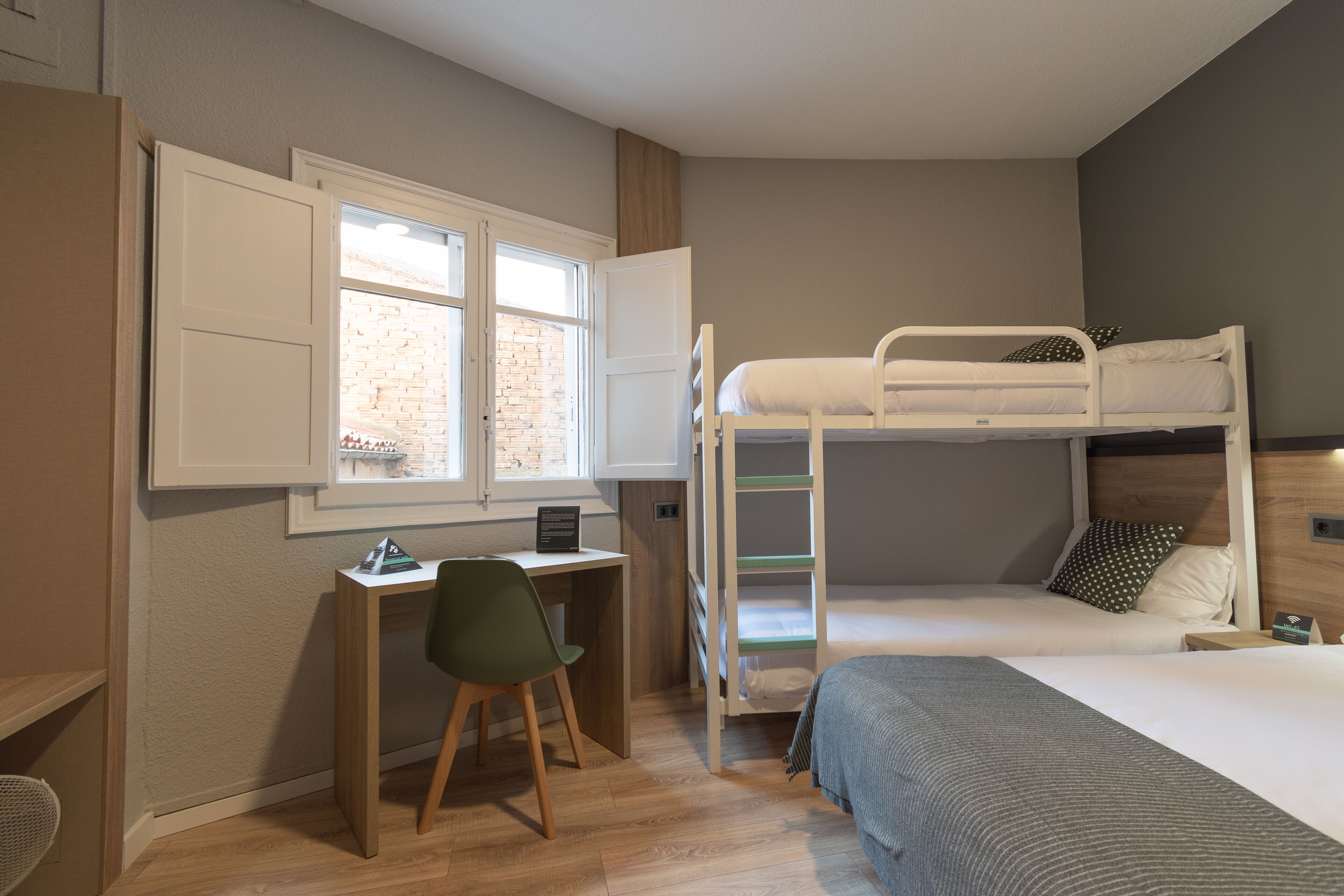 Een slaapkamer met een stapelbed, een bureau met een stoel en een raam.