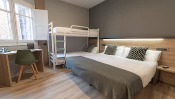 Ein modernes Hotelzimmer mit Etagenbett, Schreibtisch mit Stuhl, Nachttisch und einem Fenster mit Jalousien.