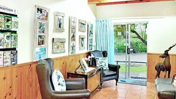 A reception area with wooden paneling, a black leather sofa, a desk with a computer, framed pictures on the wall, and a deer statue.
