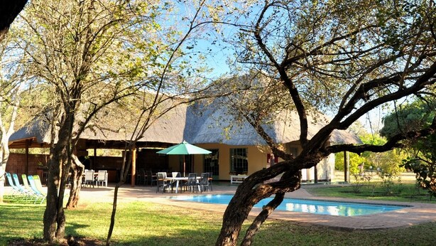 A pool area with lounge chairs, a covered seating area, and a building with a thatched roof.