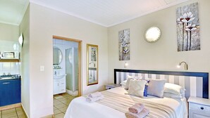 A bedroom with a bed, bedside tables, a nightstand, a mirror, and artwork on the walls.