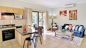 A modern kitchen with a dining area, a living room with a sofa and a coffee table, and a large window with curtains.