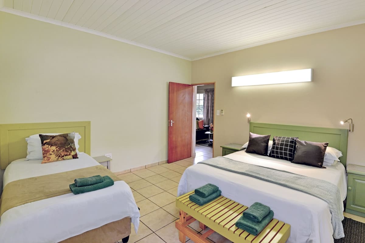 A hotel room with two beds, each with a green headboard, white bedding, and a wooden bench with towels.
