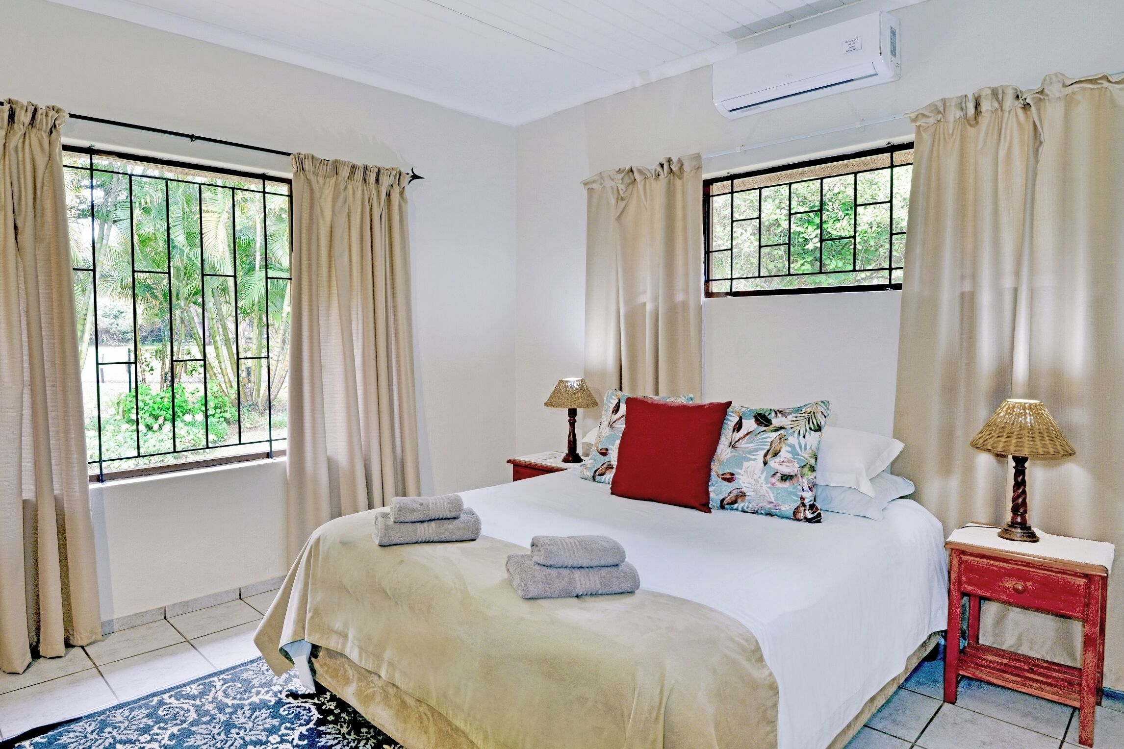 Une chambre d’hôtel avec un grand lit, deux tables de chevet, une fenêtre avec des rideaux et une vue sur la verdure.