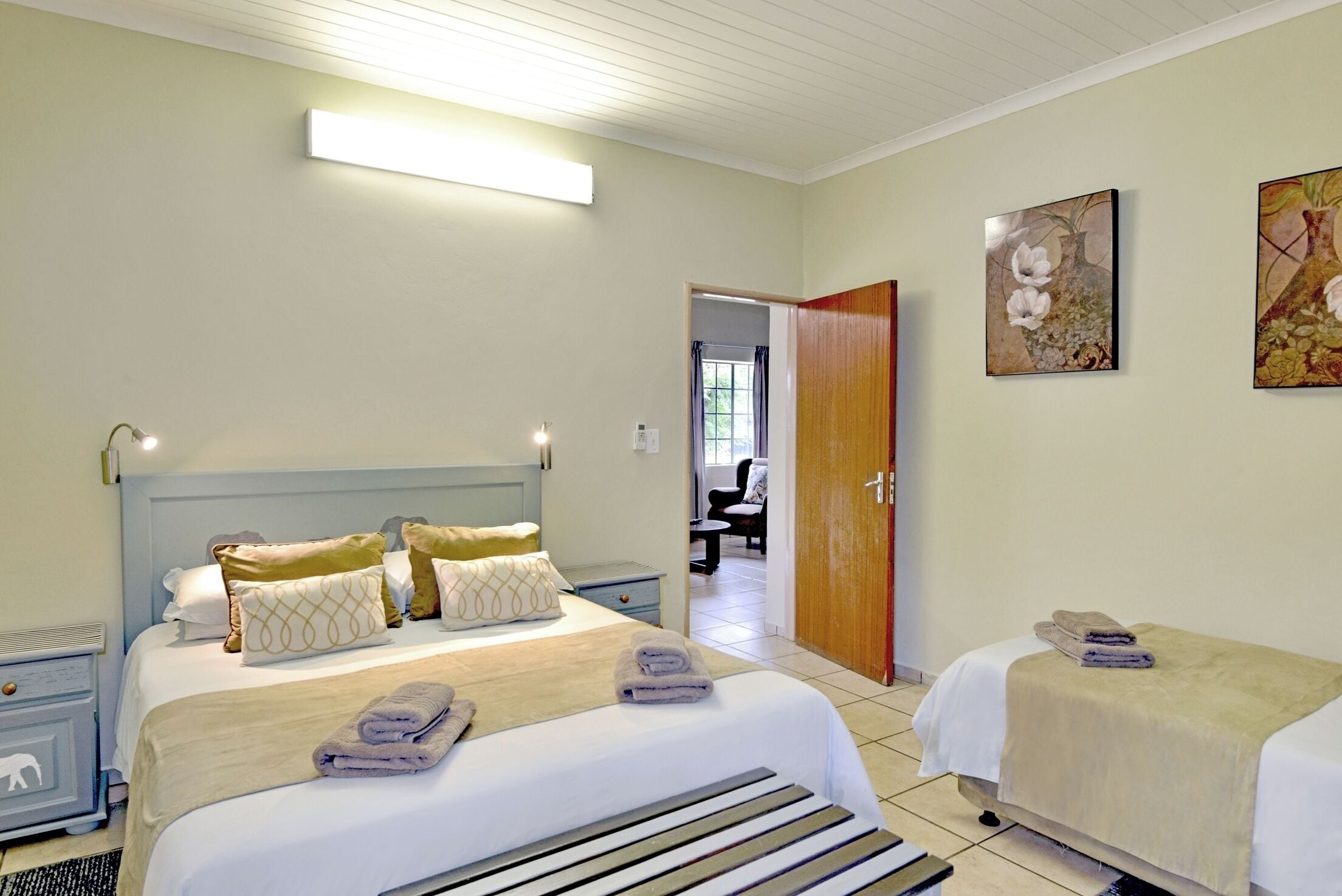 Habitación de hotel con una cama grande, una cama más pequeña, un escritorio y una silla. Se ve una puerta que da a otra habitación.