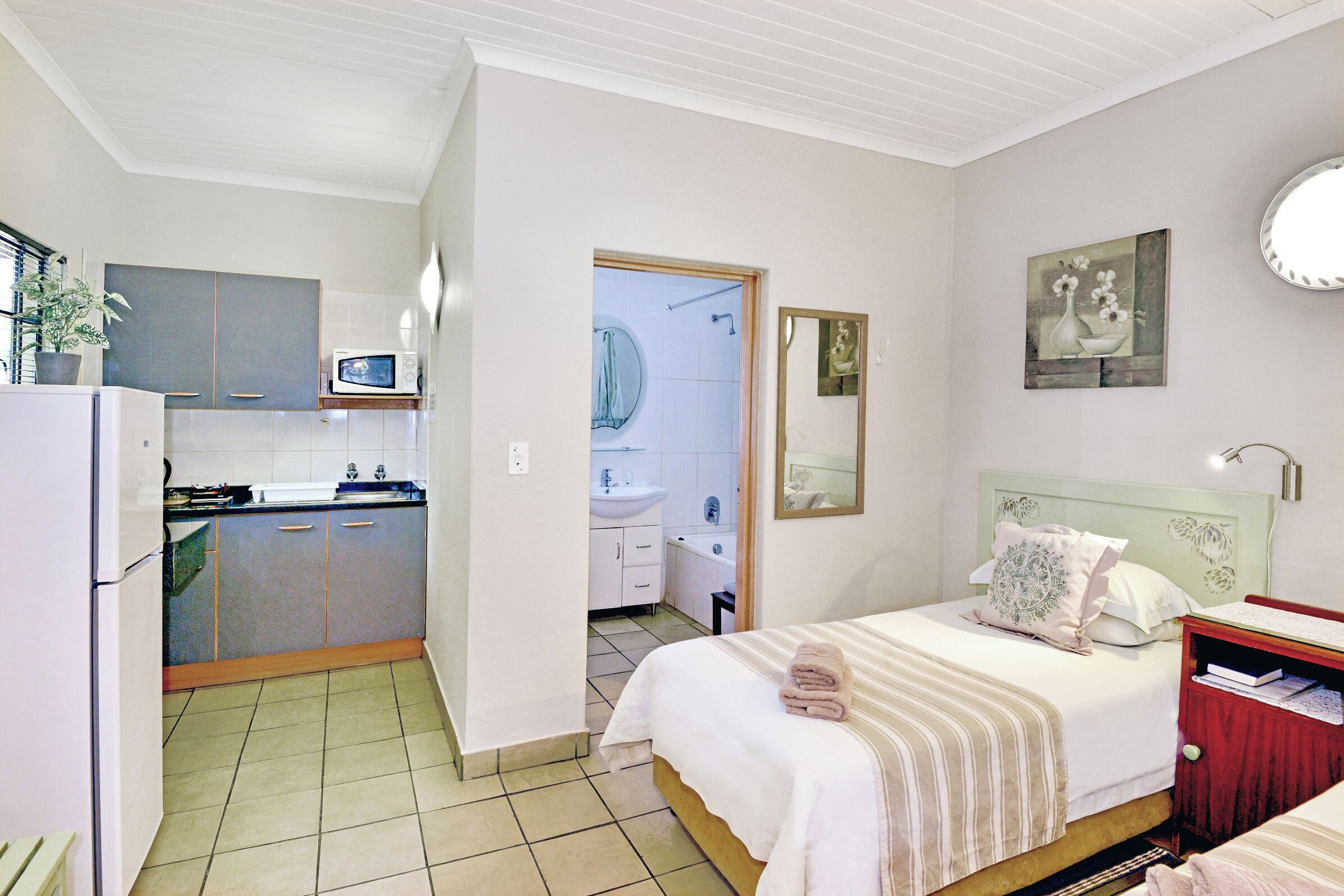 A bedroom with a bed, bedside table, and a view into the kitchen.