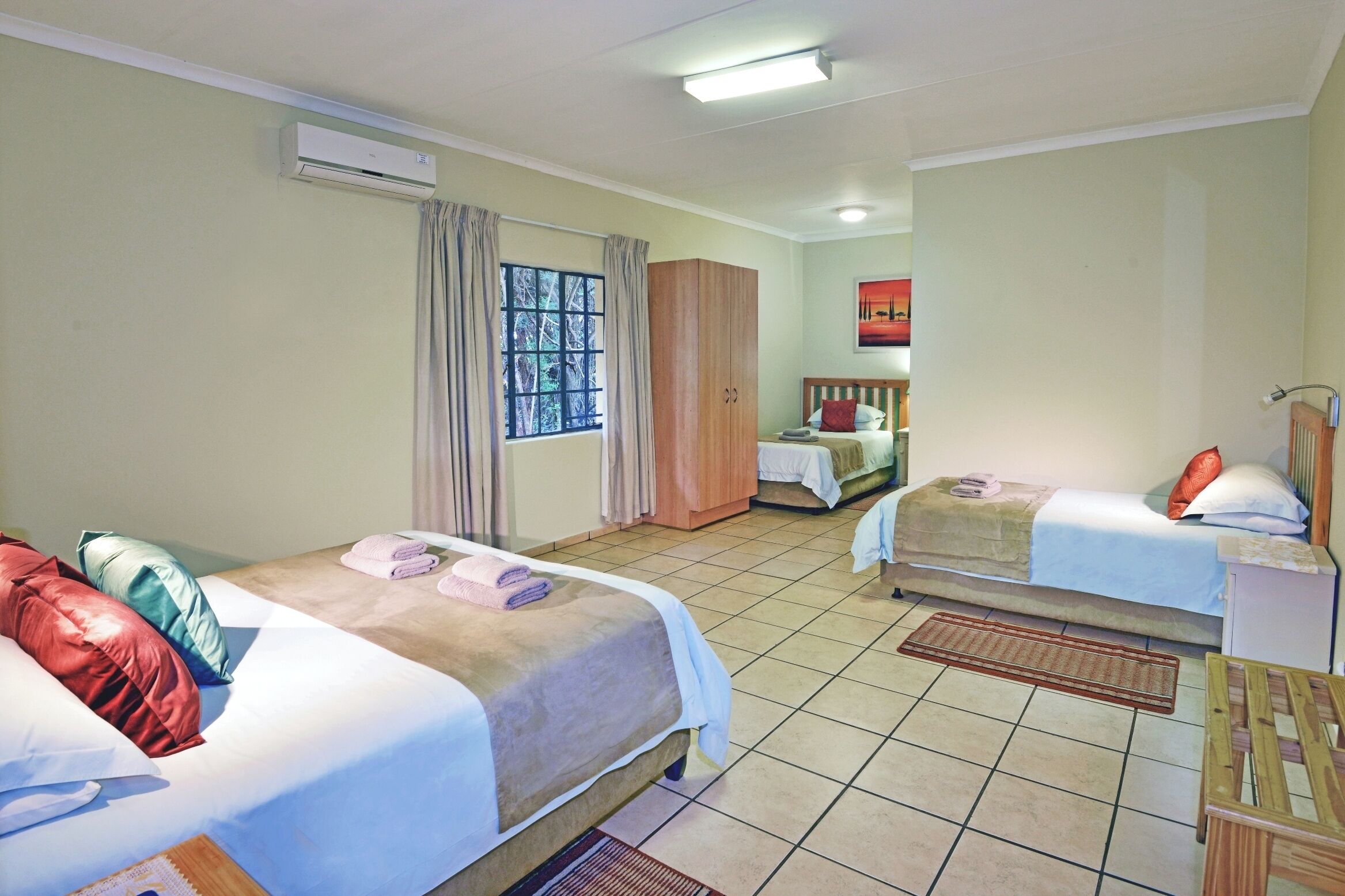 A hotel room with two beds, a wardrobe, a desk, and a window with curtains.