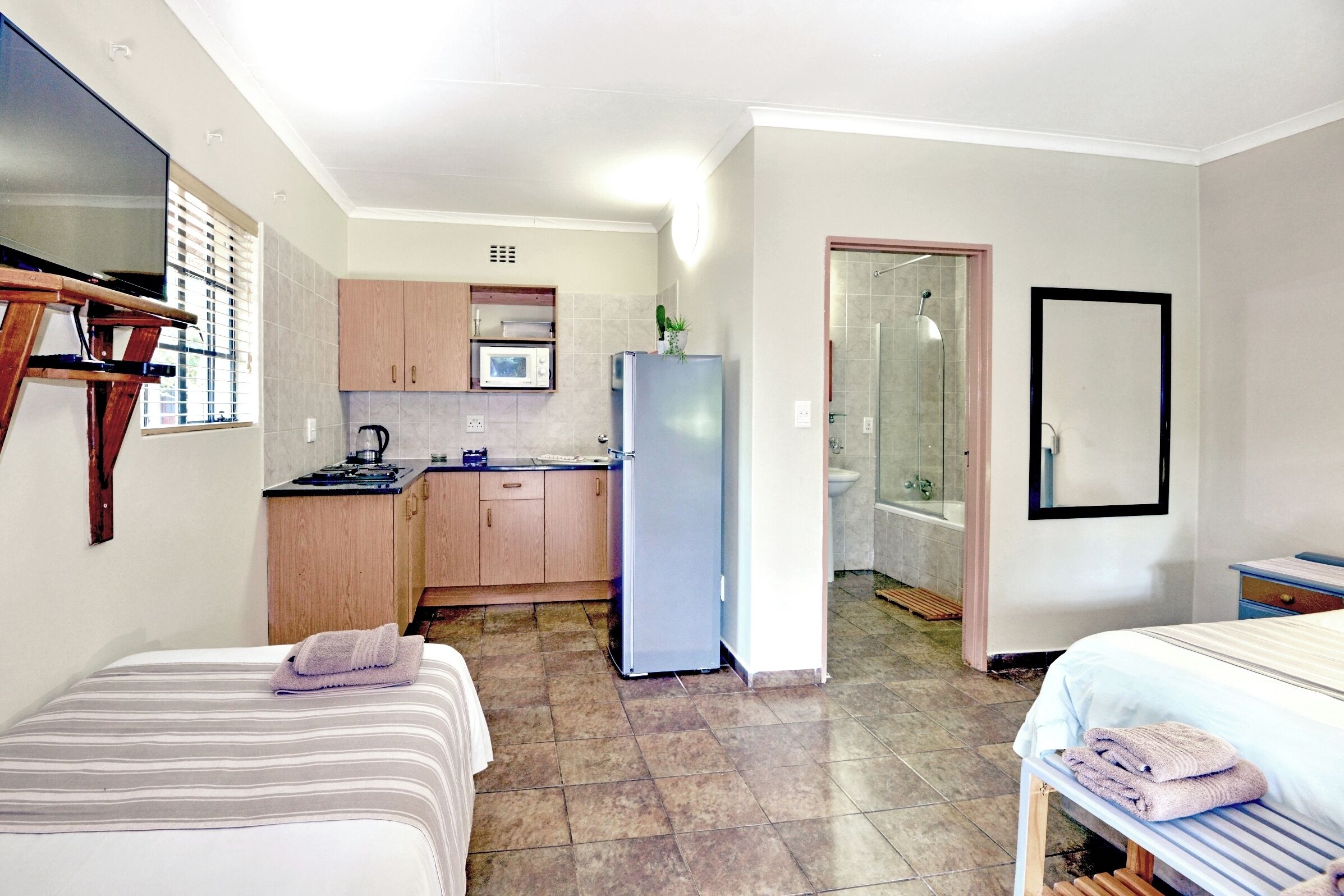 A compact hotel room with a bed, a small desk, a kitchenette with a microwave, and a bathroom with a shower.