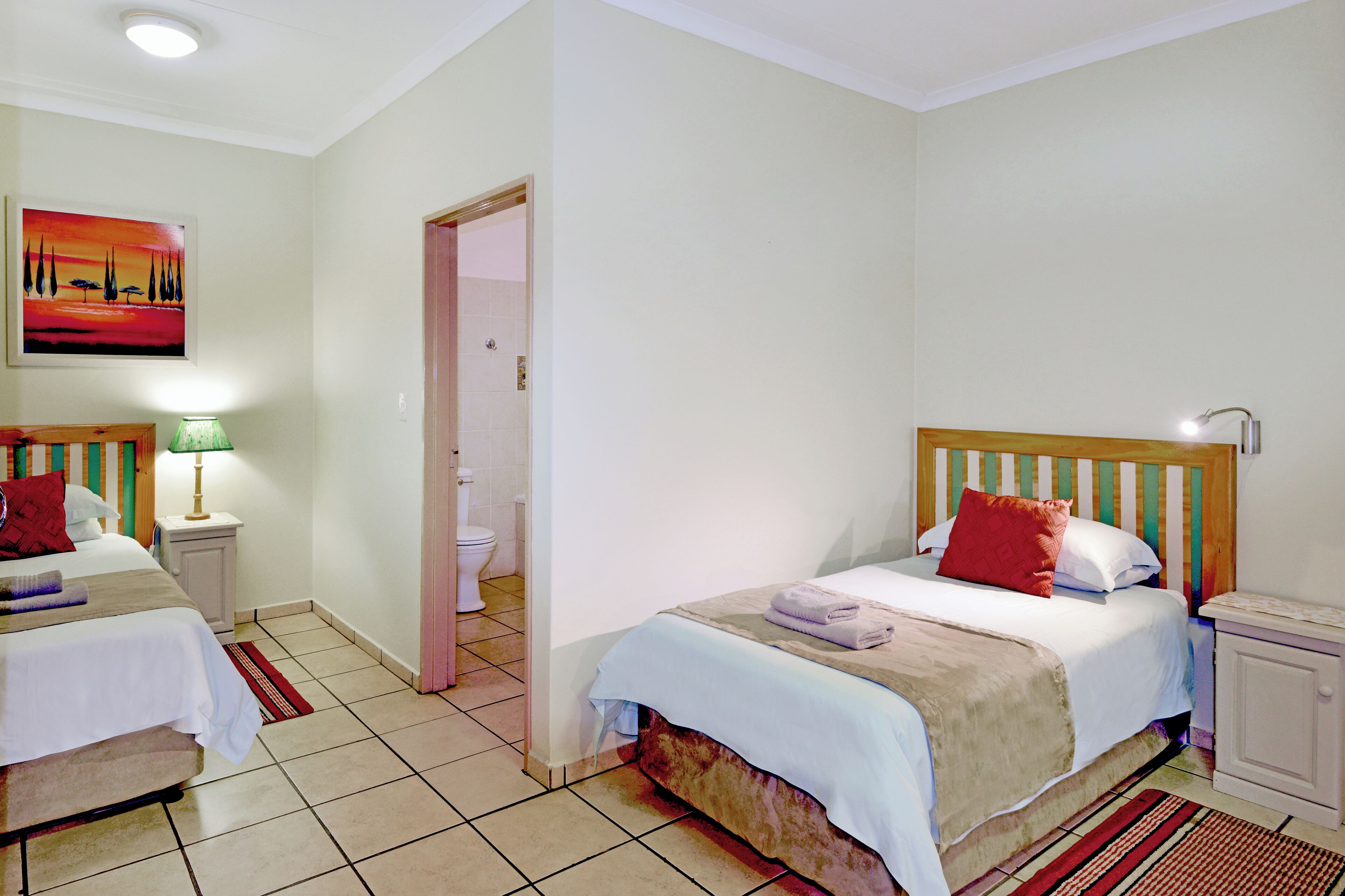 A hotel room with two beds, a bathroom, and a painting on the wall.