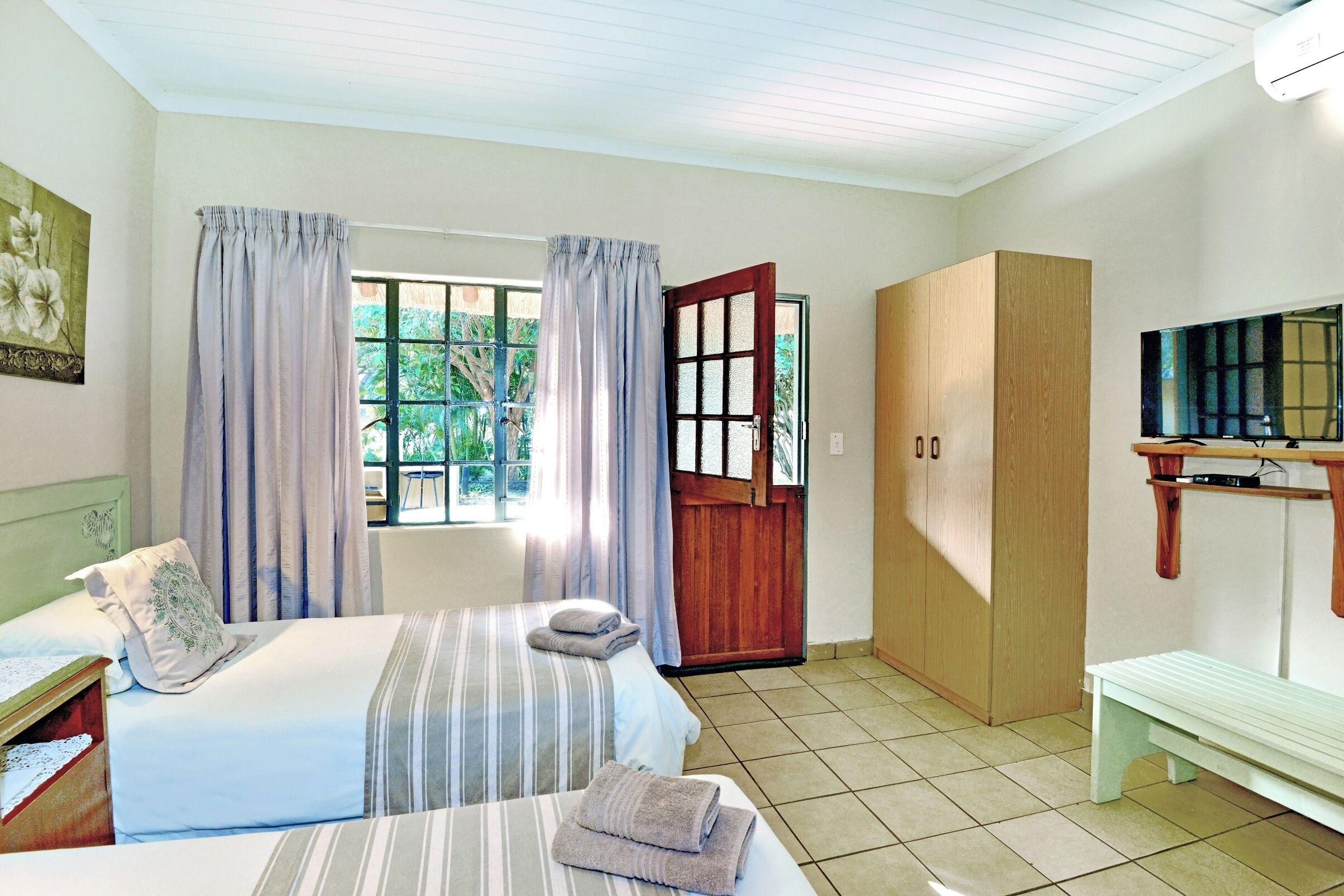 A room with two beds, a wardrobe, a television, and a bench.