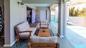 Una sala moderna con un sofá, sillones y una mesa de centro. Hay un ventanal corredero que da a un espacio exterior con piscina.
