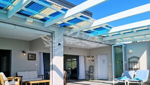 Un área de piscina con una piscina azul cristalina, sillas de descanso y una pérgola con paneles azules y blancos.