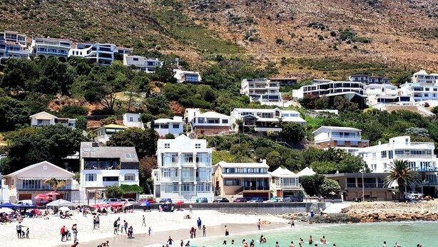 Zona costera con playa, gente nadando y edificios en una ladera.