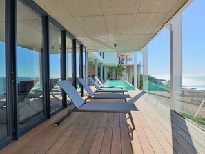 Una terraza de madera con tumbonas y una piscina, con vistas al mar.