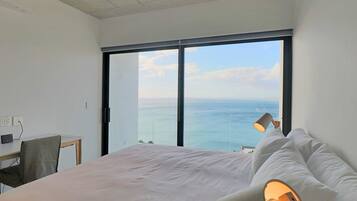 A bedroom with a large bed, a desk, and a view of the sea through a large window.