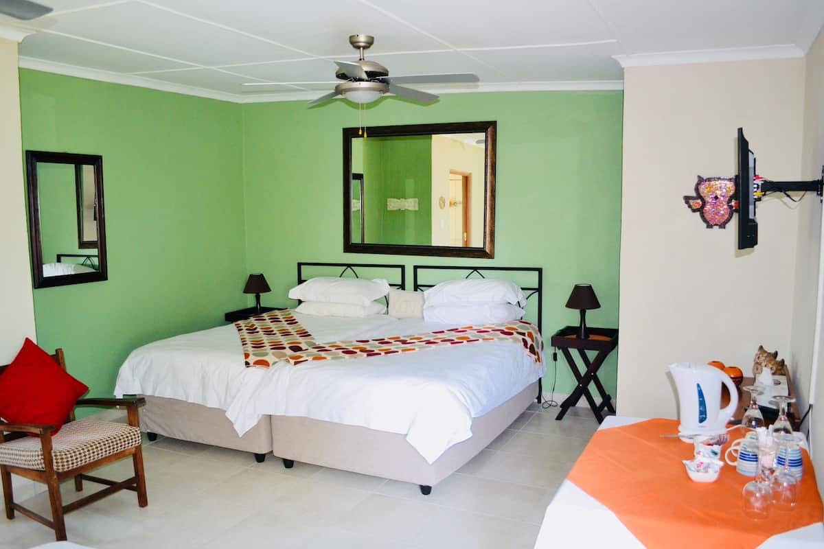 A bedroom with a bed, two bedside tables, a chair, a ceiling fan, a mirror, and a wall-mounted TV.