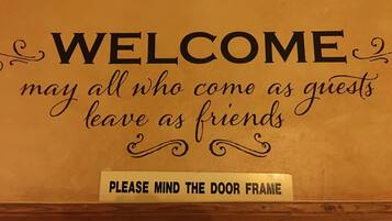 A sign with the text "WELCOME may all who come as guests leave as friends" and "PLEASE MIND THE DOOR FRAME".