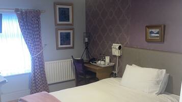 A bedroom with a bed, a desk, a chair, a radiator, and a window with curtains.