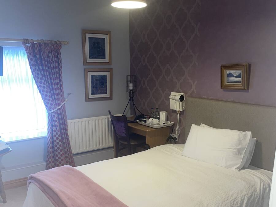Une chambre à coucher comprenant un lit, un bureau, une chaise, un radiateur et une fenêtre avec des rideaux.