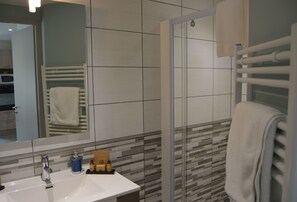 Une salle de bain moderne avec un lavabo blanc, une douche en verre et un mur recouvert de carreaux.