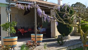 Un bâtiment doté d’un toit recouvert de tuiles, d’un espace extérieur aménagé pour s’asseoir et de plantes en pot.