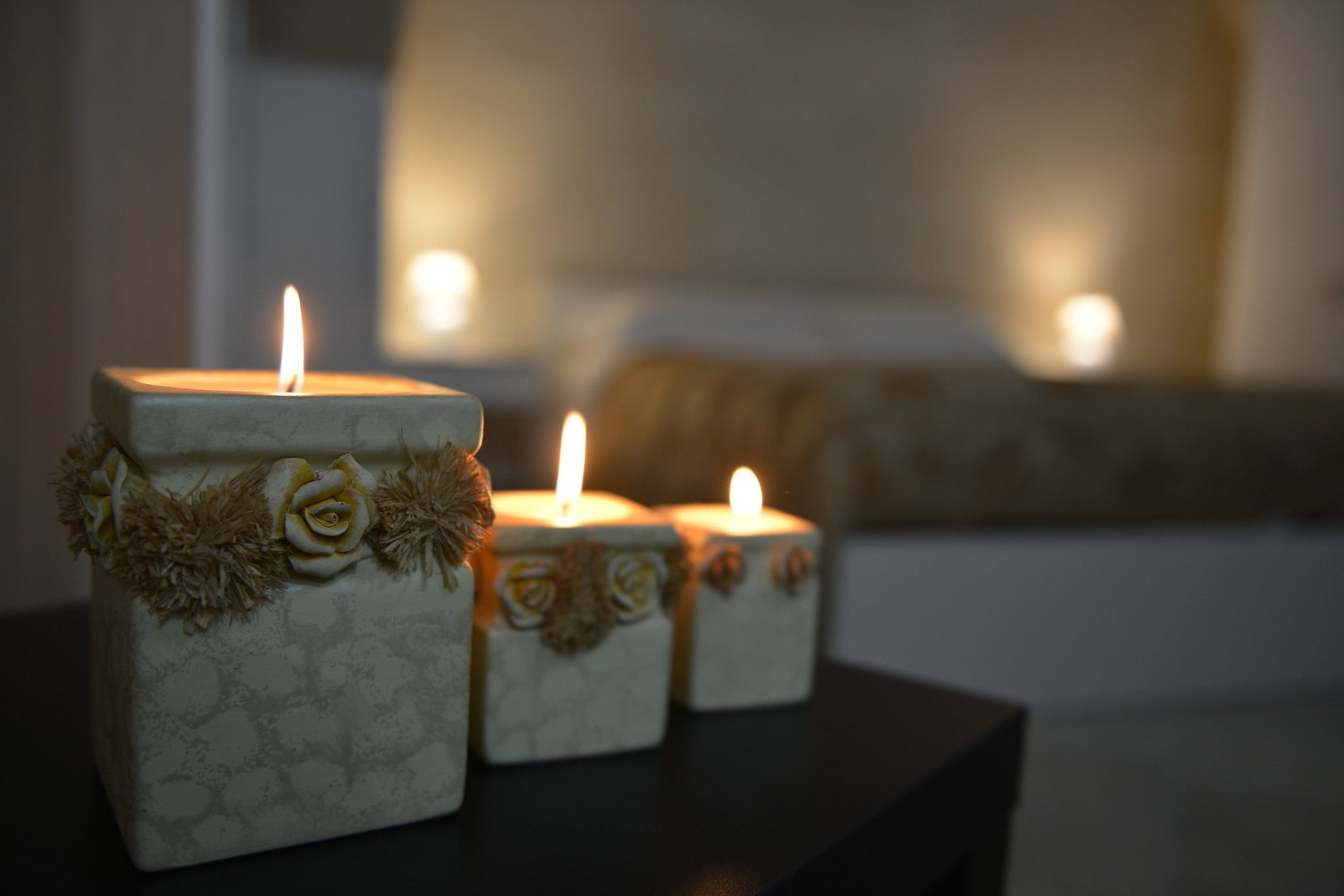 Three square candles with floral decorations on a dark surface.