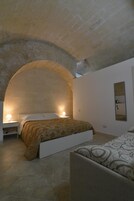 Una camera da letto con un letto sotto un soffitto in pietra ad arco, un comodino con una lampada e uno specchio fissato alla parete.