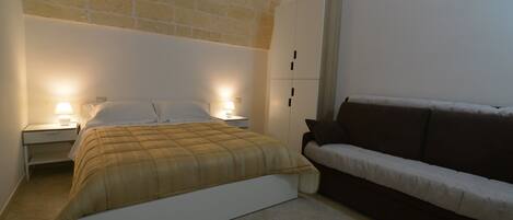 Un dormitorio con cama, mesitas de noche, un sofá y un armario.