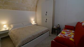 A bedroom with a bed, a wardrobe, a nightstand, a red sofa, and a lamp.