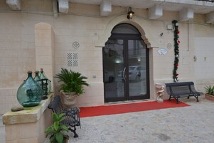 L'ingresso di un edificio con porta in vetro, piante in vaso, una panchina e elementi decorativi.