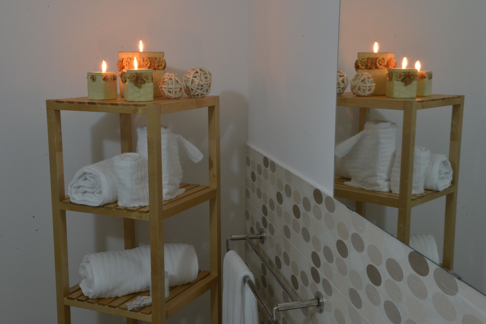 Un baño con repisas de madera que sostienen toallas dobladas y velas con diseños florales.