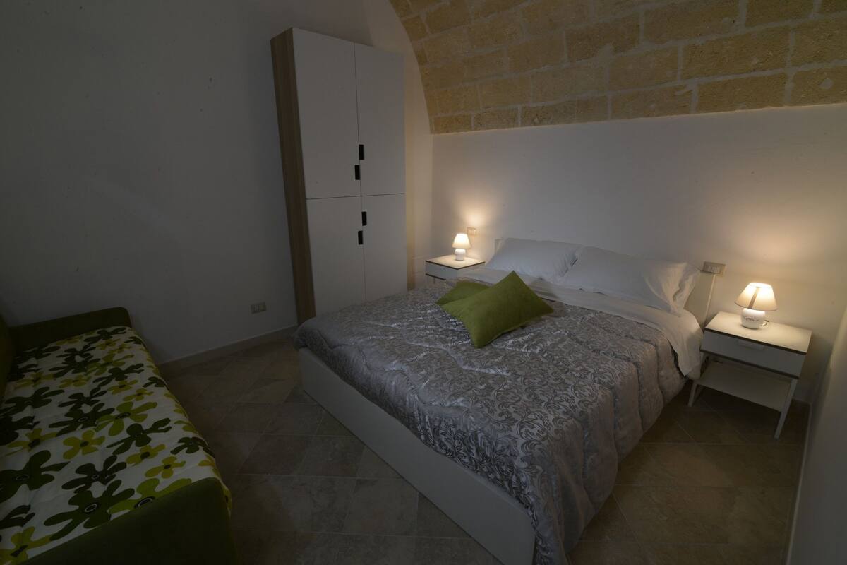 A bedroom with a bed, two bedside tables with lamps, a wardrobe, and a small table with a lamp.