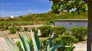 A landscaped garden with a tennis court, a small building, and a hill in the background. - Domaine Bocca Di Feno (Bonifacio)