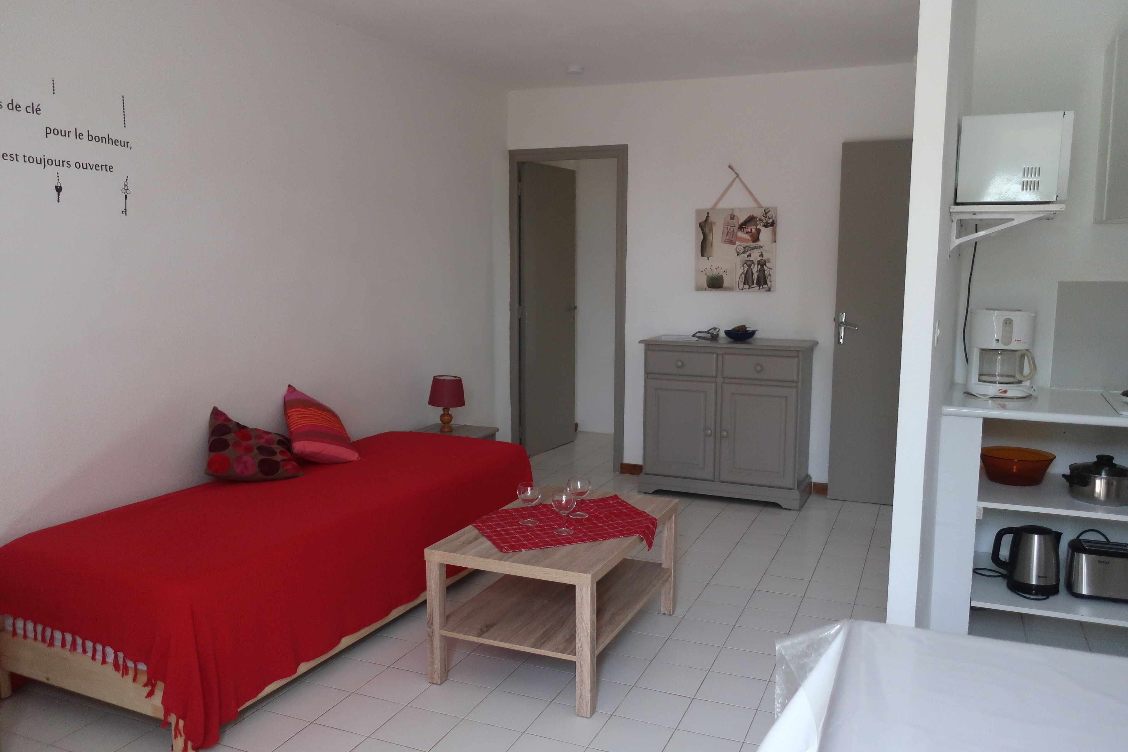 A small, well-lit room with a bed, a table, and a kitchenette.