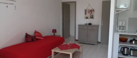 A small, well-lit room with a bed, a table, and a kitchenette.