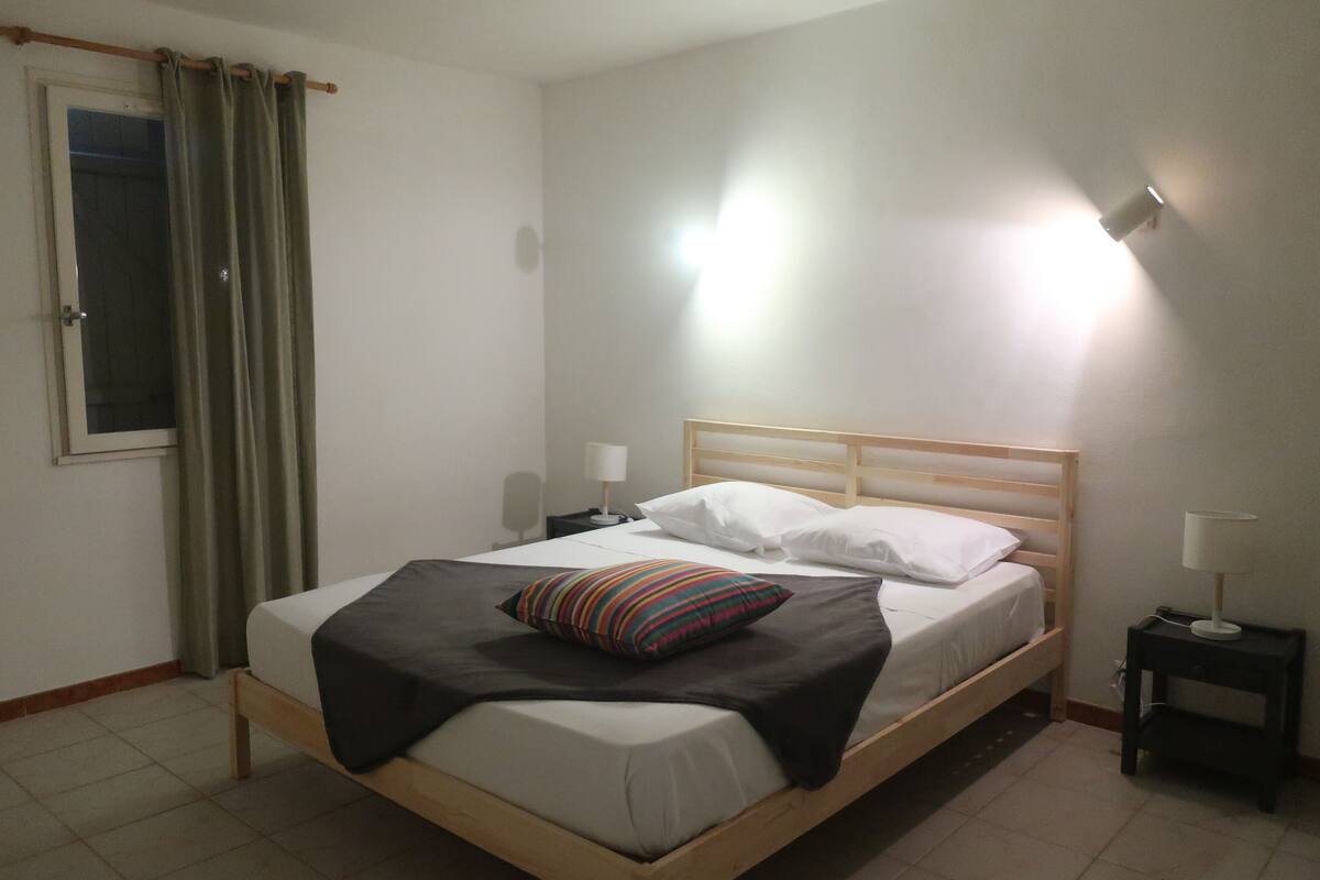 A single bed with a wooden frame, a bedside table with a lamp, and a window with curtains.