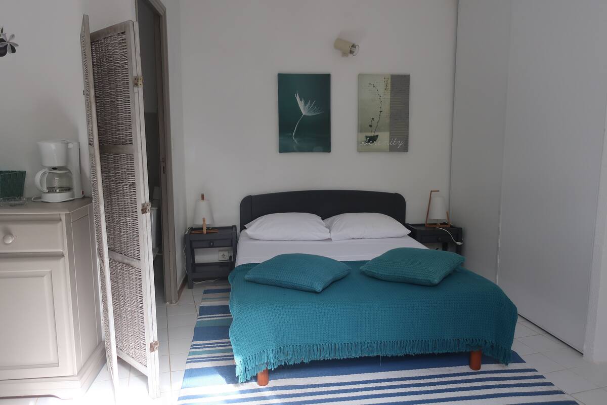 A bedroom with a bed, a nightstand, a coffee maker, and a door.