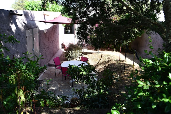 An outdoor patio area with a round table and chairs, surrounded by plants and a stone wall. - Domaine Bocca Di Feno (Bonifacio)