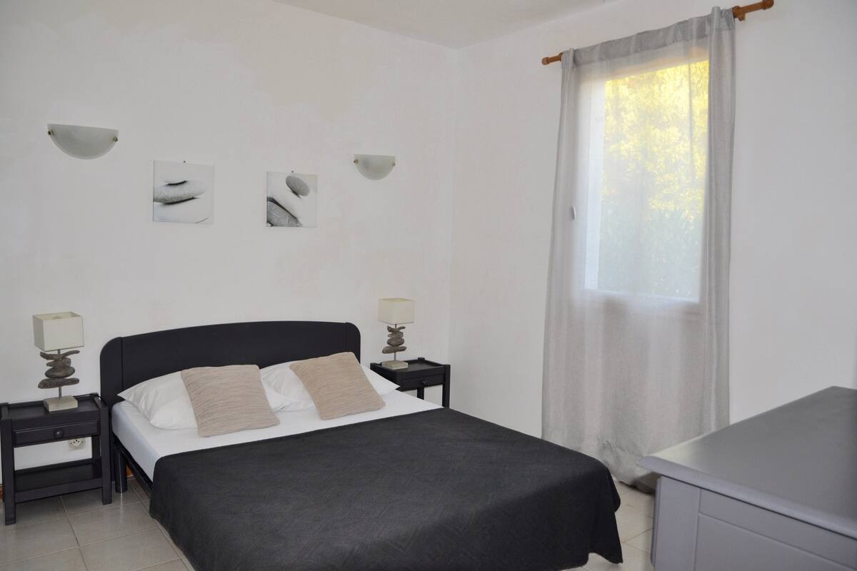 A bedroom with a bed, two bedside tables, a desk, and a window with curtains.