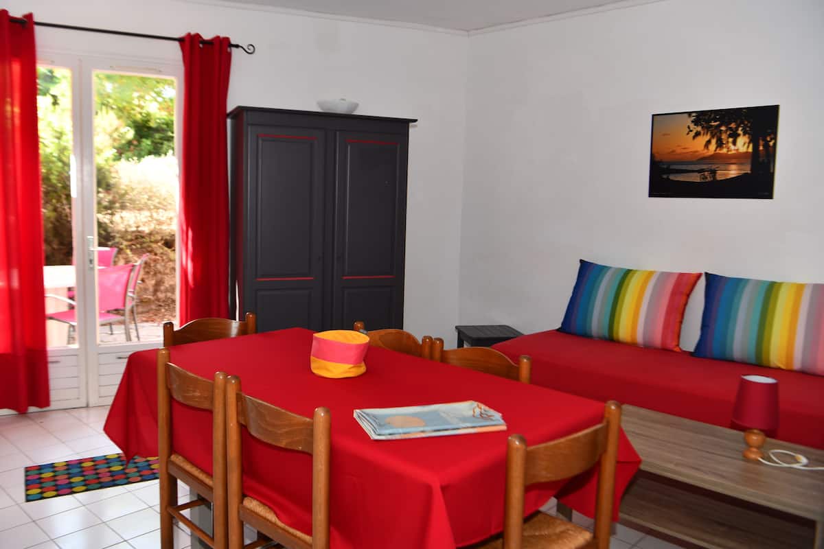 A room with a dining table and chairs, a sofa with colorful cushions, a cabinet, and a painting on the wall.