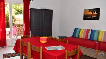 A room with a dining table and chairs, a sofa with colorful cushions, a cabinet, and a painting on the wall.