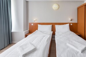 A hotel room with two single beds, a wooden headboard, bedside lamps, a wall clock, and a window with curtains. - Elizeu Hotel (Bucharest)