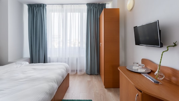 A hotel room with a bed, a desk with a flat-screen TV, a wardrobe, and a window with curtains. - Elizeu Hotel (Bucharest)